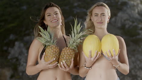 Glückliche-Frauen-Mit-Ananas-Und-Melonen-Im-Bikini-Am-Strand